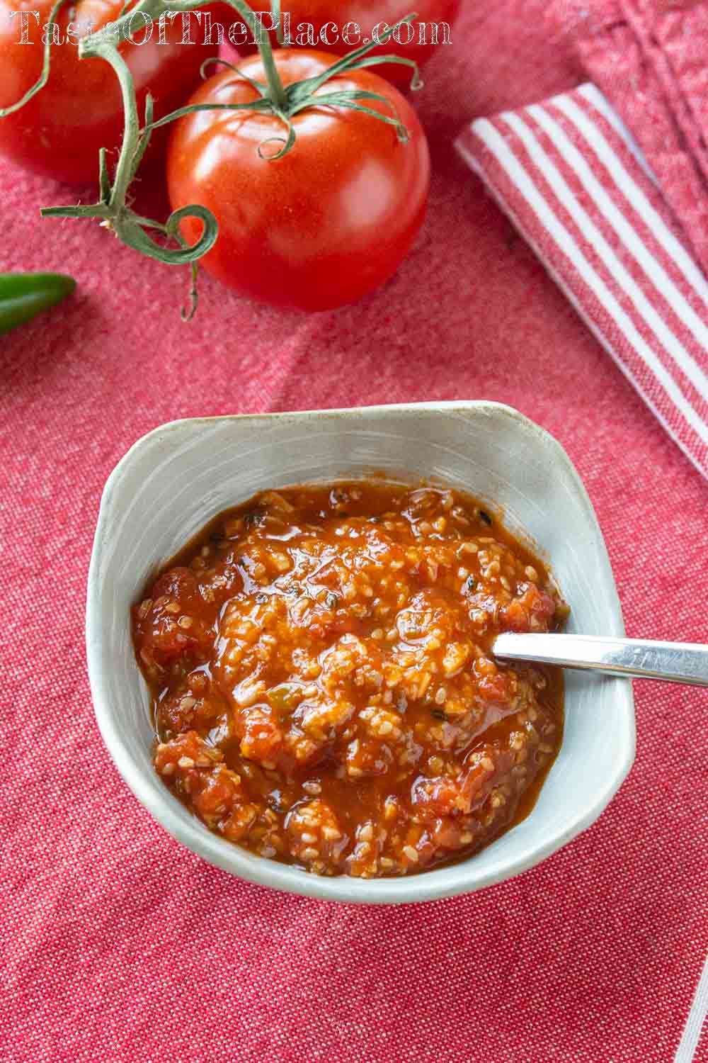 Tomato chutney with tomatoes and a pepper in the background